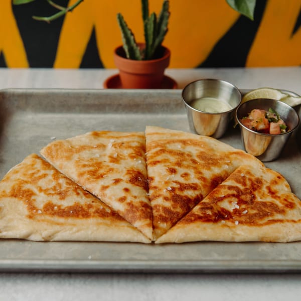 Golden-brown quesadilla cut into triangles, served with salsa and crema on a metal tray.