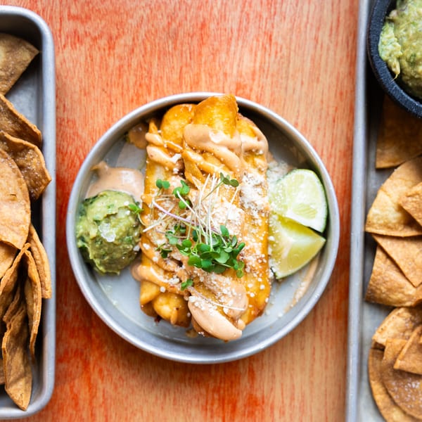 Hombre y Lobo's golden taquitos with sauce, guacamole, lime, and tortilla chips on a wooden table.