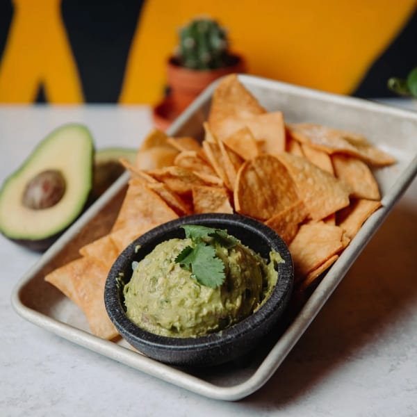 Guacamole with cilantro and tortilla chips on a metal tray, with a halved avocado.