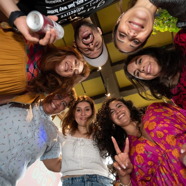 Seven smiling friends looking down into the camera, one holding a drink can.