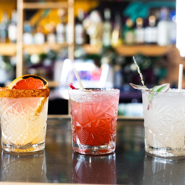 Three colorful Mexican cocktails, including a grapefruit margarita, on a dark bar top.