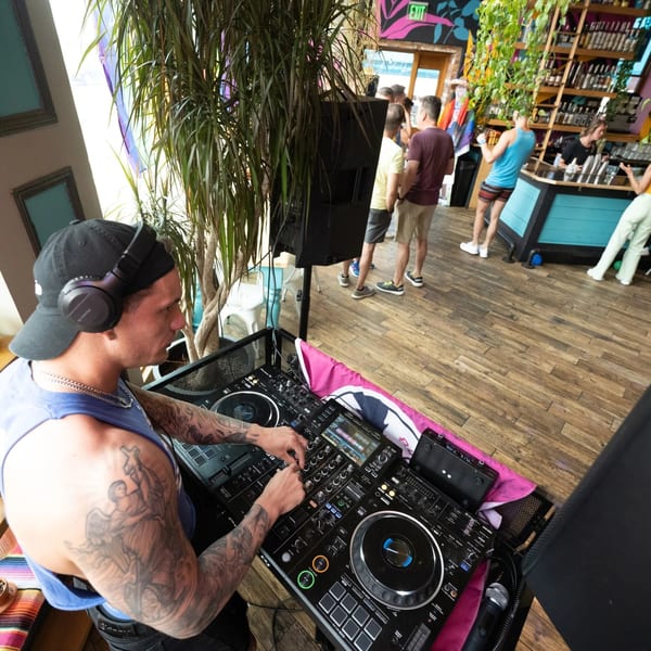 DJ with headphones and tattoos mixing music at a lively Hombre y Lobo restaurant event.