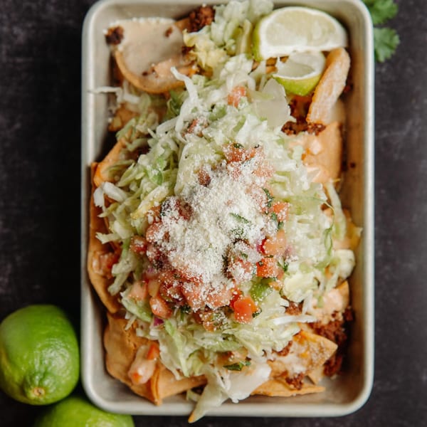 Overhead view of a metal tray filled with Hombre y Lobo's Mexican nachos, topped with lettuce, pico de gallo, and cheese.